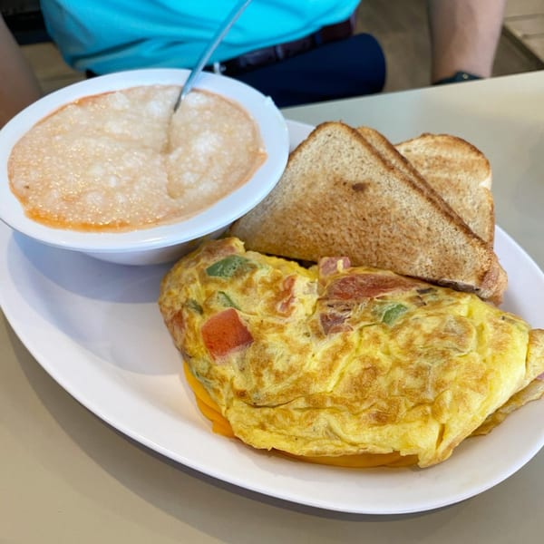 A southern breakfast plate with a vegetable omelet, toast, and a bowl of grits.