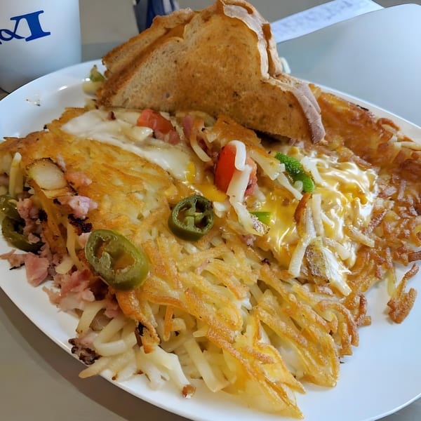 A southern breakfast skillet with hash browns, melted cheese, ham, jalapeños, and toast on a white plate.